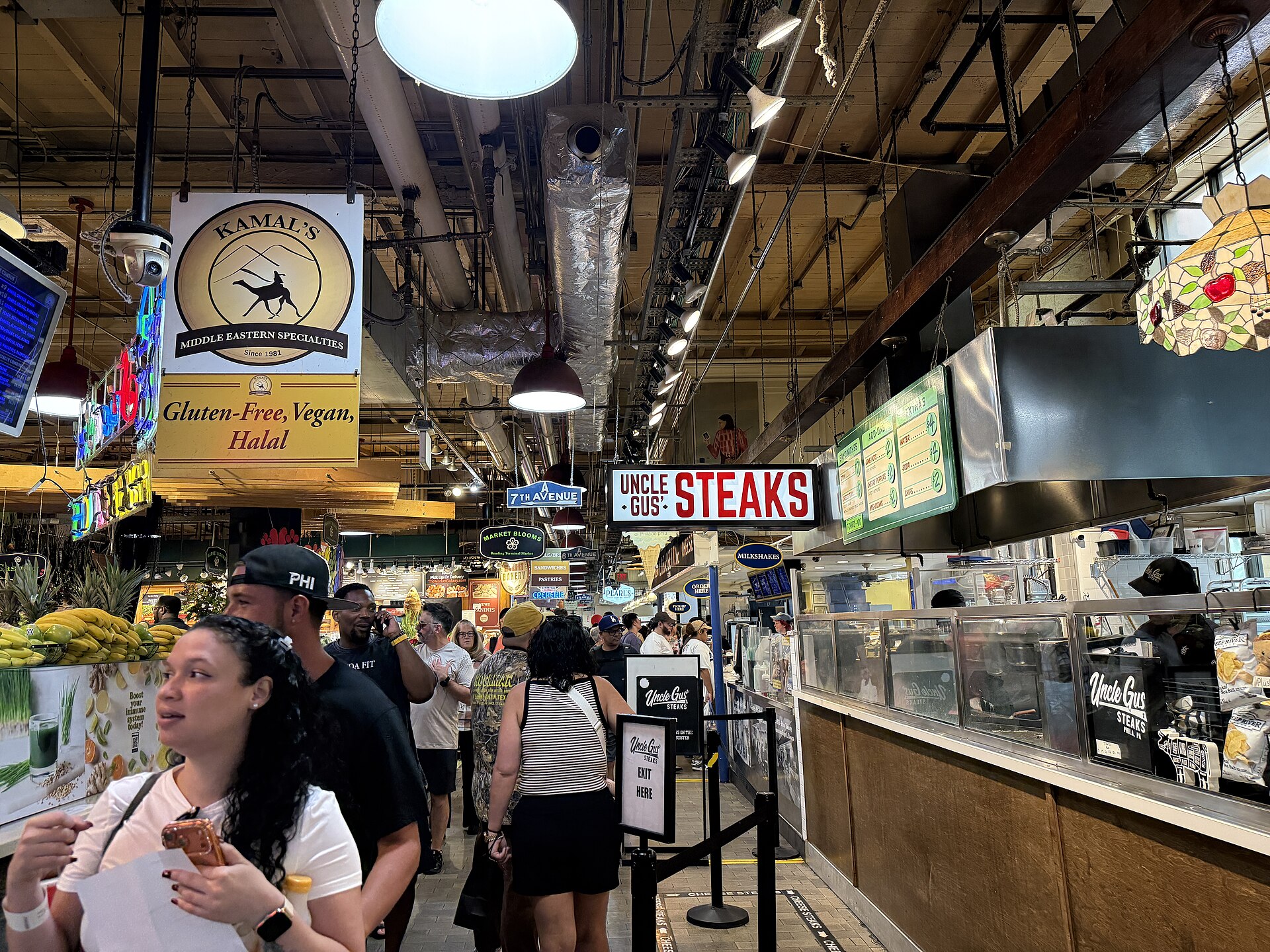 Посетители меѓу тезгите со храна и натписите во Reading Terminal Market во Филаделфија